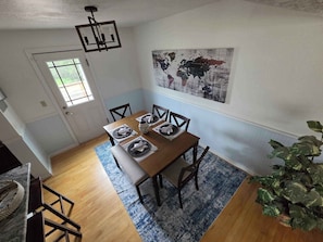 Un coin repas avec une table en bois dressée pour quatre personnes, une carte du monde accrochée au mur et une grande plante dans un coin.