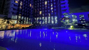 A multi-story hotel with a pool reflecting blue lights.