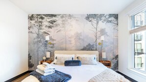 A bedroom with a large bed, two bedside tables with lamps, a wall mural, and a window with a view. - Designer Apt: Walk to Busch Stadium, Free Parking (St. Louis)
