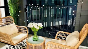 A cozy outdoor seating area with wicker chairs and a patterned rug, a glass vase with white flowers, and string lights. - Designer Apt: Walk to Busch Stadium, Free Parking (St. Louis)