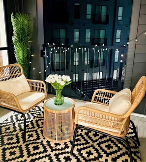 A cozy outdoor seating area with wicker chairs and a patterned rug, a glass vase with white flowers, and string lights. - Designer Apt: Walk to Busch Stadium, Free Parking (St. Louis)