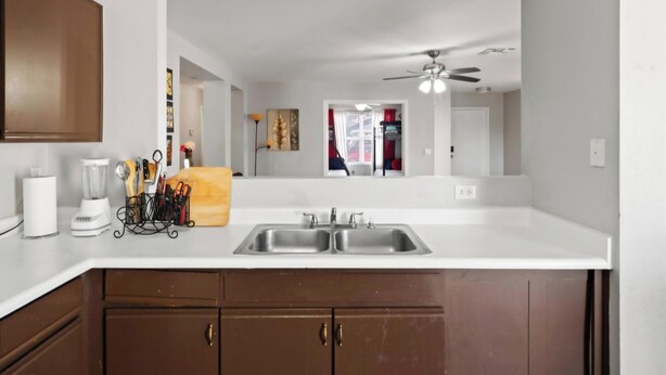 A kitchen with a double sink, wooden cabinets, a ceiling fan, and a view into the adjacent room. - Lovely 3-bedroom estate with AC in beautiful El Mirage (El Mirage)