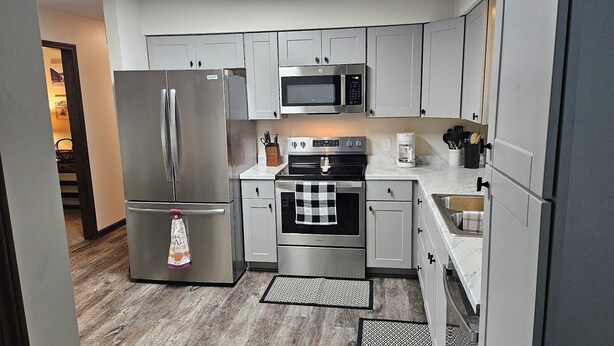 A modern kitchen with stainless steel appliances, white cabinetry, and a checkered oven towel. - Whole House - Sleeps 6 - Remodeled Kitchen & Bath - Near I-90 - North Side Jvl (Janesville)