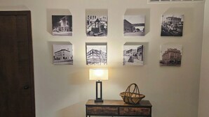 A wall with eight black and white photographs of buildings and streets. Below the photos, there's a wooden table with a lamp and a wicker basket. - Whole House - Sleeps 6 - Remodeled Kitchen & Bath - Near I-90 - North Side Jvl (Janesville)