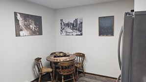 A dining area with a round wooden table, four chairs, and a refrigerator. There are two black-and-white photographs on the walls. - Whole House - Sleeps 6 - Remodeled Kitchen & Bath - Near I-90 - North Side Jvl (Janesville)