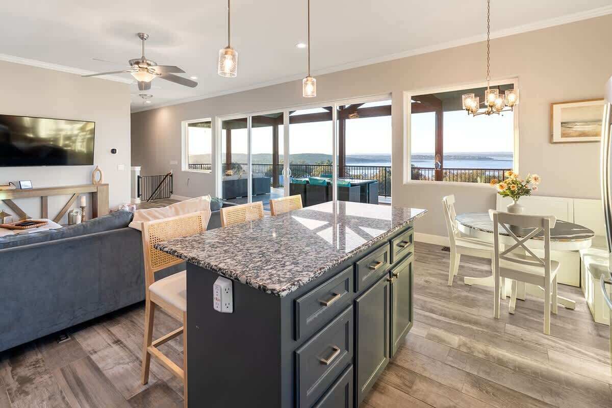 A modern kitchen with a large island, a dining area with a table and chairs, a sofa, and a TV mounted on the wall.