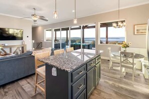 Una cocina moderna con una isla grande, un área de comedor con mesa y sillas, un sofá y un televisor montado en la pared.