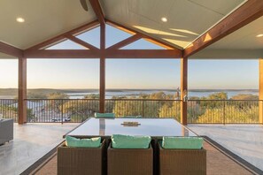 A covered outdoor seating area with a table and chairs, a view of the landscape, and a balcony railing.