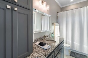 A bathroom with a granite countertop, a sink, a mirror, a toilet, and a shower curtain.