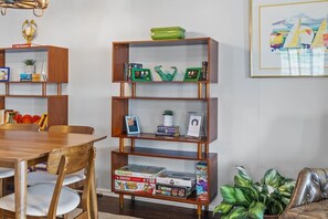 Ein Essbereich mit Holztisch und -stühlen, einem Bücherregal mit diversen Gegenständen und einem gerahmten Bild an der Wand.