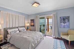 Ein Schlafzimmer mit Bett, Sessel, Nachttisch, Lampe, Fenster und Blick ins Freie.