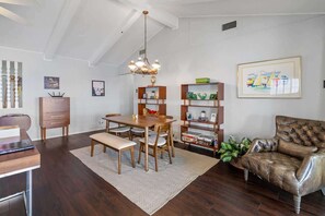 Un comedor con una mesa y sillas de madera, un banco, una araña y una estantería con diversos objetos.