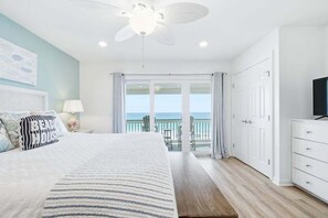 Ein Schlafzimmer mit Bett, Deckenventilator, Nachttisch, Lampe, Fernseher, Kommode und einem Balkon mit Meerblick.