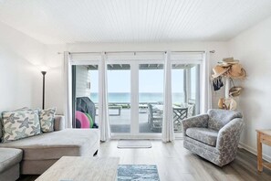 Een woonkamer met een bank, fauteuil en uitzicht op de oceaan door grote glazen deuren.