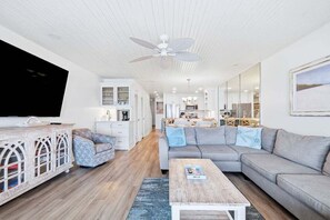 A modern living room with a flat-screen TV, a ceiling fan, a grey sofa, and a wooden coffee table. - Beachfront, Decks, Cloud Nine, Sleeps 12, 30A (Inlet Beach)