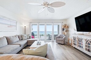 En stue med sofa, lænestol, sofabord, fjernsyn og havudsigt gennem store skydedøre.