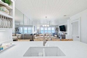 Et moderne køkken med en stor ø-vask, et spiseområde med et rundt bord og en opholdsstue med fjernsyn og siddepladser.