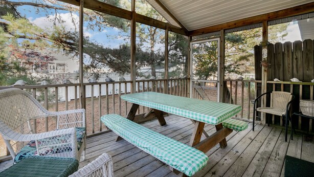 Un patio techado al aire libre con una mesa y bancos de madera, rodeado por un cerco de madera y árboles.