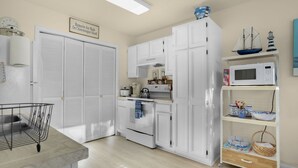 Una cocina con armarios blancos, microondas, estufa y una repisa con adornos.