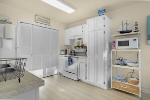 A kitchen with white cabinets, a microwave, a stove, and a shelf with decorative items. - Half Shell | Clean accommodations close to Beach Road! (Chincoteague Island)