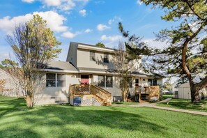 A two-story house with a front porch, a small deck, and a covered outdoor area. - Half Shell | Clean accommodations close to Beach Road! (Chincoteague Island)