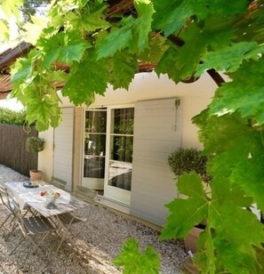 A patio with a table and chairs, a small potted plant, and a white building with a sliding door.