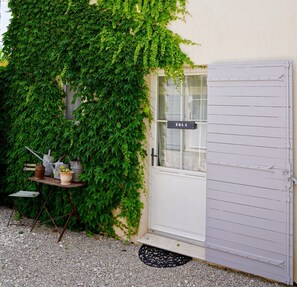 A white door with a window, a small table with pots, and a gravel path.