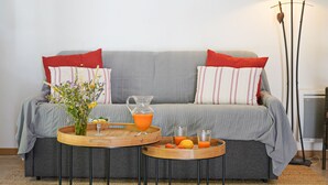 A living room with a grey sofa, red and white striped pillows, a wooden coffee table with a vase of flowers, a glass pitcher of orange juice, and a floor lamp.
