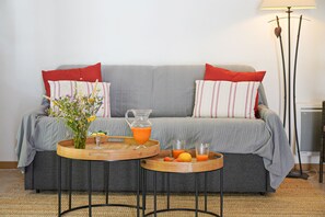 A living room with a grey sofa, red and white striped pillows, a wooden coffee table with a vase of flowers, a glass pitcher of orange juice, and a floor lamp.