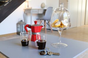 A table with a coffee maker, two cups of coffee, a glass with lemon slices, and a set of keys.