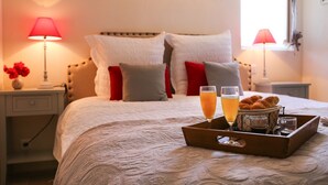 A neatly made bed with pillows, a tray with croissants, glasses of orange juice, and a vase of flowers.
