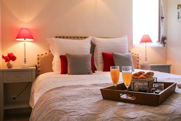 A neatly made bed with pillows, a tray with croissants, glasses of orange juice, and a vase of flowers.