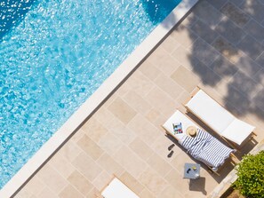 An aerial view of a swimming pool with tiled flooring, two sun loungers, and a small table with a magazine.