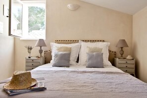 A bedroom with a bed, two bedside tables, a window, and a hat on the bed.