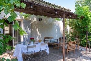 An outdoor patio with a table set for dining, a wooden bench, and a pergola overhead.
