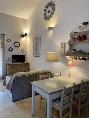 Una sala de estar con televisor, sofá, mesa de comedor, sillas, un reloj en la pared y adornos.