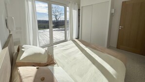 A bedroom with a large bed, a wooden door, and a view of a rural landscape through a sliding glass door. - Le Pavillon blanc - CAHUZAC-SUR-VERE (CAHUZAC-SUR-VERE)