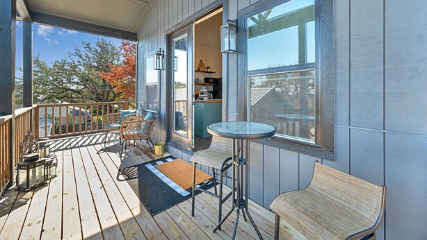 Une terrasse en bois avec des sièges d’extérieur, une porte vitrée donnant sur une cuisine et une vue sur les arbres.