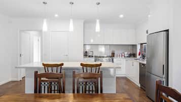 A modern kitchen with white cabinets, a stainless steel refrigerator, and a wooden dining table with chairs.