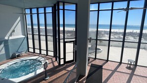 Un balcón con bañera de hidromasaje, ventanas amplias y vista a la playa.