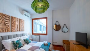 A bedroom with a bed, a television on a wooden cabinet, a window with a view, and wall-mounted artwork. - Trastevere 8 Guests Apartaments WIFI (Roma)