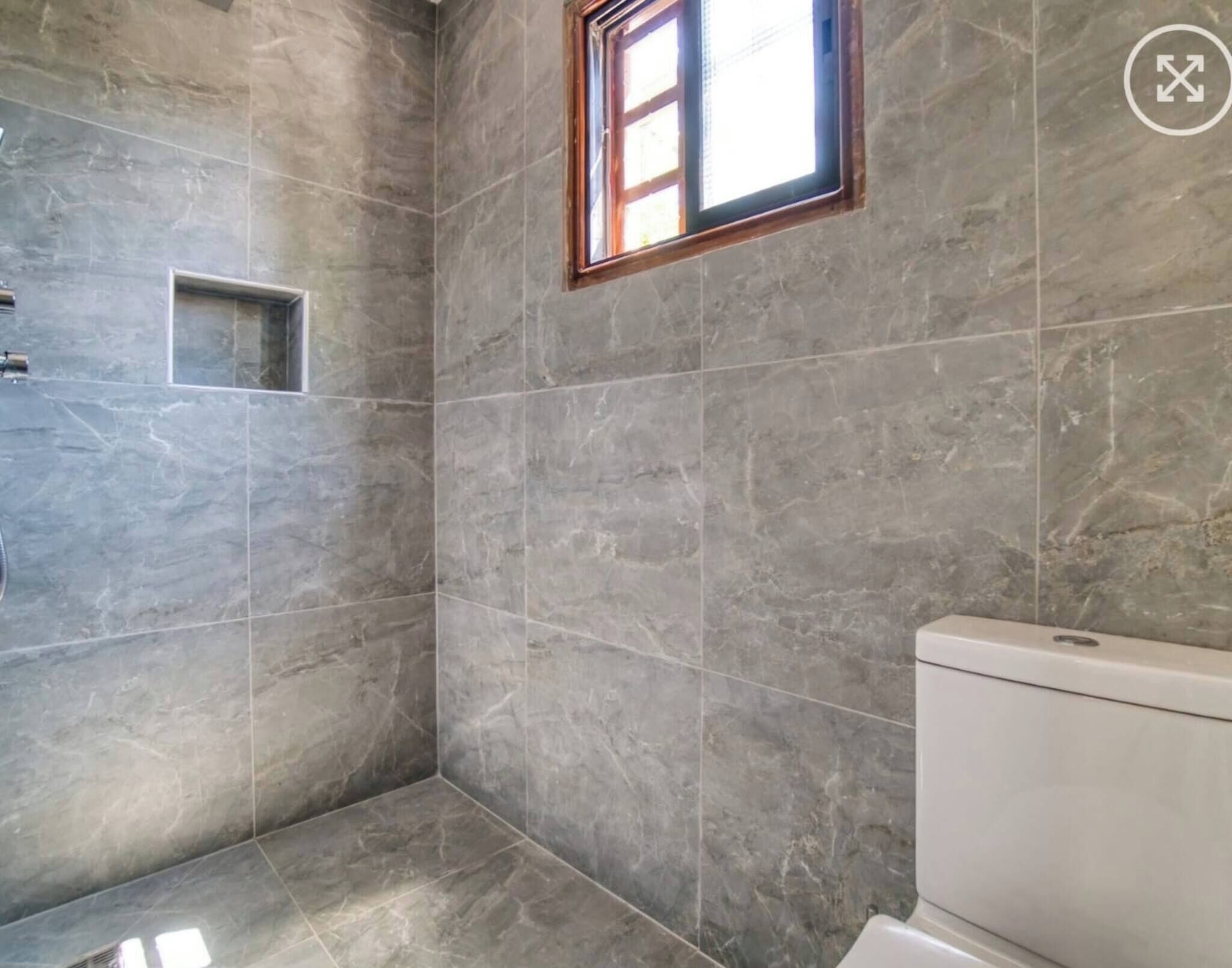 A bathroom with grey marble tiles, a window, and a toilet.