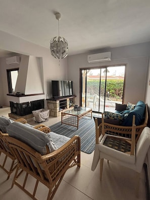 A living room with wicker furniture, a television, and a fireplace. - The Tala Townhouse Pafos (Tala)
