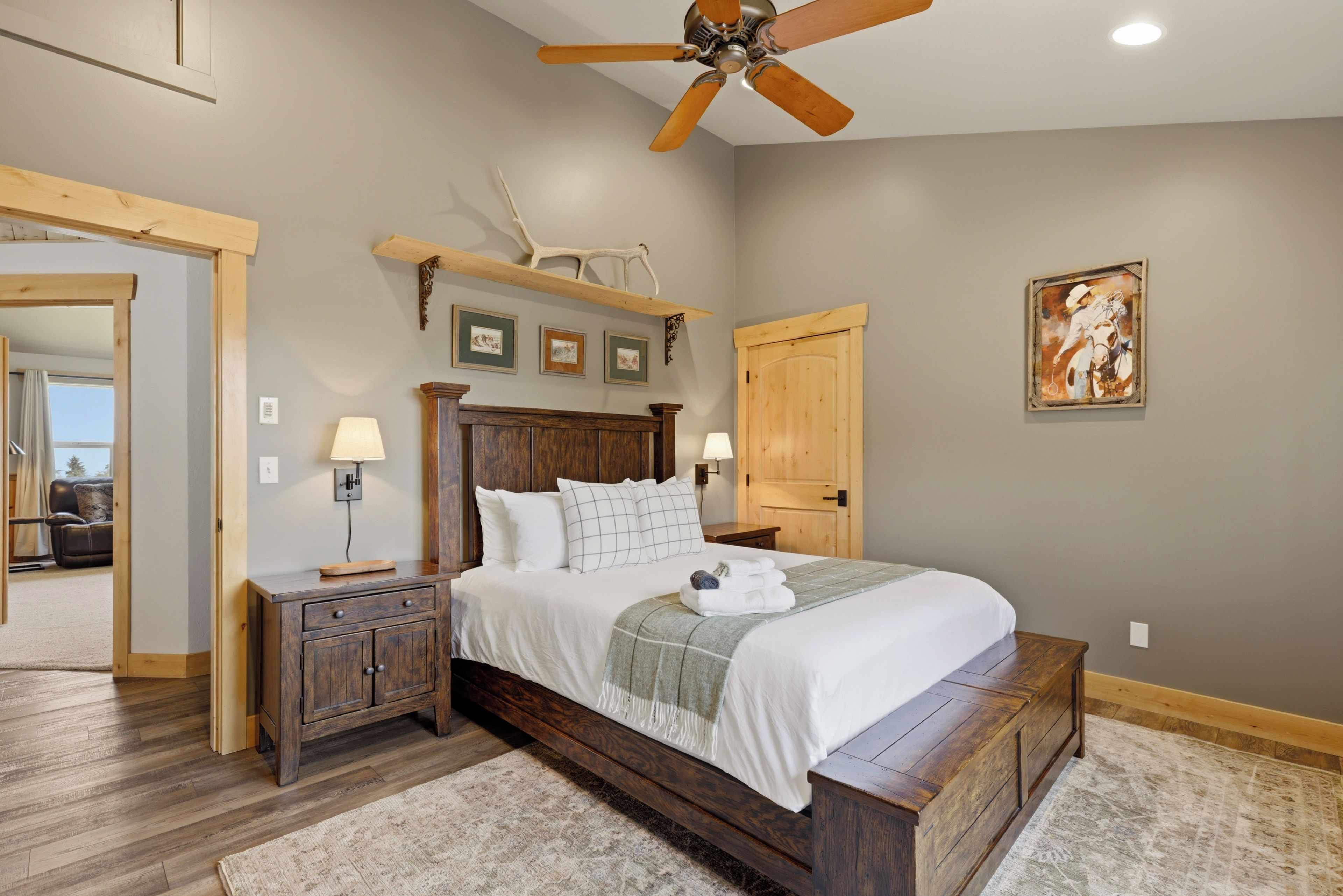 A bedroom with a wooden bed, a ceiling fan, a painting, and a door.