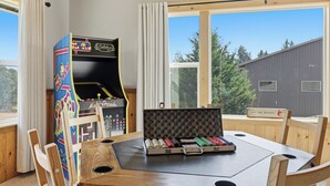 Ein Zimmer mit einem Holztisch, einem farbenfrohen Spielautomaten und einem Fenster mit Blick auf Bäume und ein Gebäude.