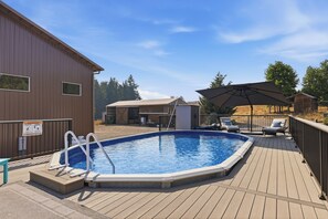 Una piscina amb una zona de solàrium, una zona coberta amb caires i un edifici de fusta al fons.