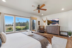 Ein Schlafzimmer mit einem großen Bett, einem Deckenventilator, Blick ins Freie, einem Kamin und einem aufgehängten Hirschkopf.