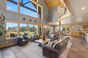 Amplia sala de estar con ventanas grandes, chimenea y cocina con armarios de madera.