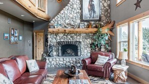 A rustic interior with a stone fireplace, leather sofas, and a wooden staircase. - Roosters Coop - Wine Country at a Rustic, Lodge Style Retreat with Hot Tub & Pool (Newberg)