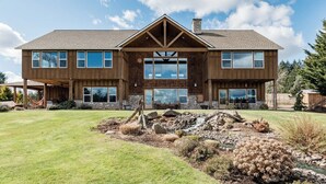 A two-story wooden house with a stone foundation, large windows, and a covered patio area. - Roosters Coop - Wine Country at a Rustic, Lodge Style Retreat with Hot Tub & Pool (Newberg)